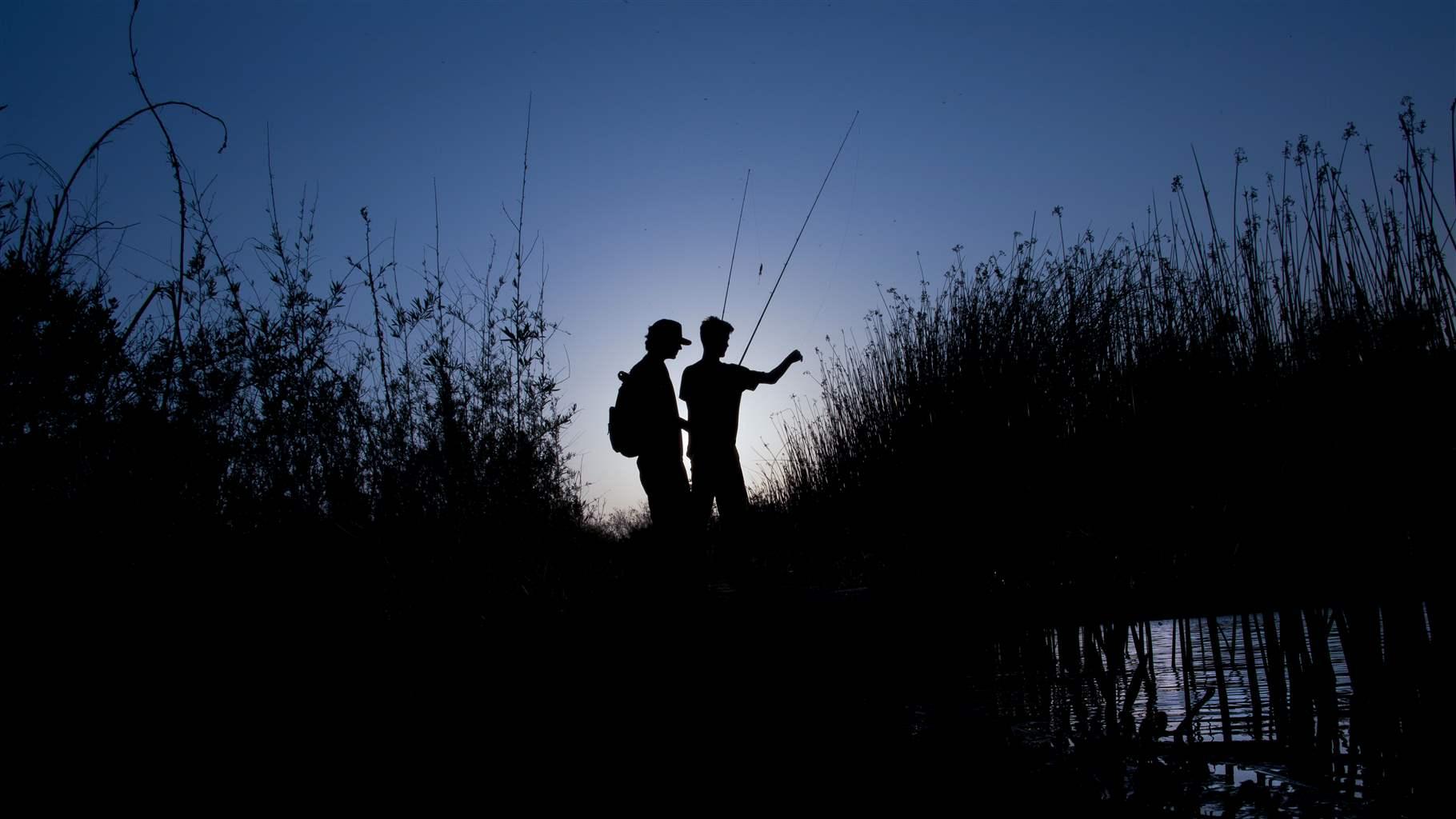 The silhouette of two figures in a boat, fishing rods poised