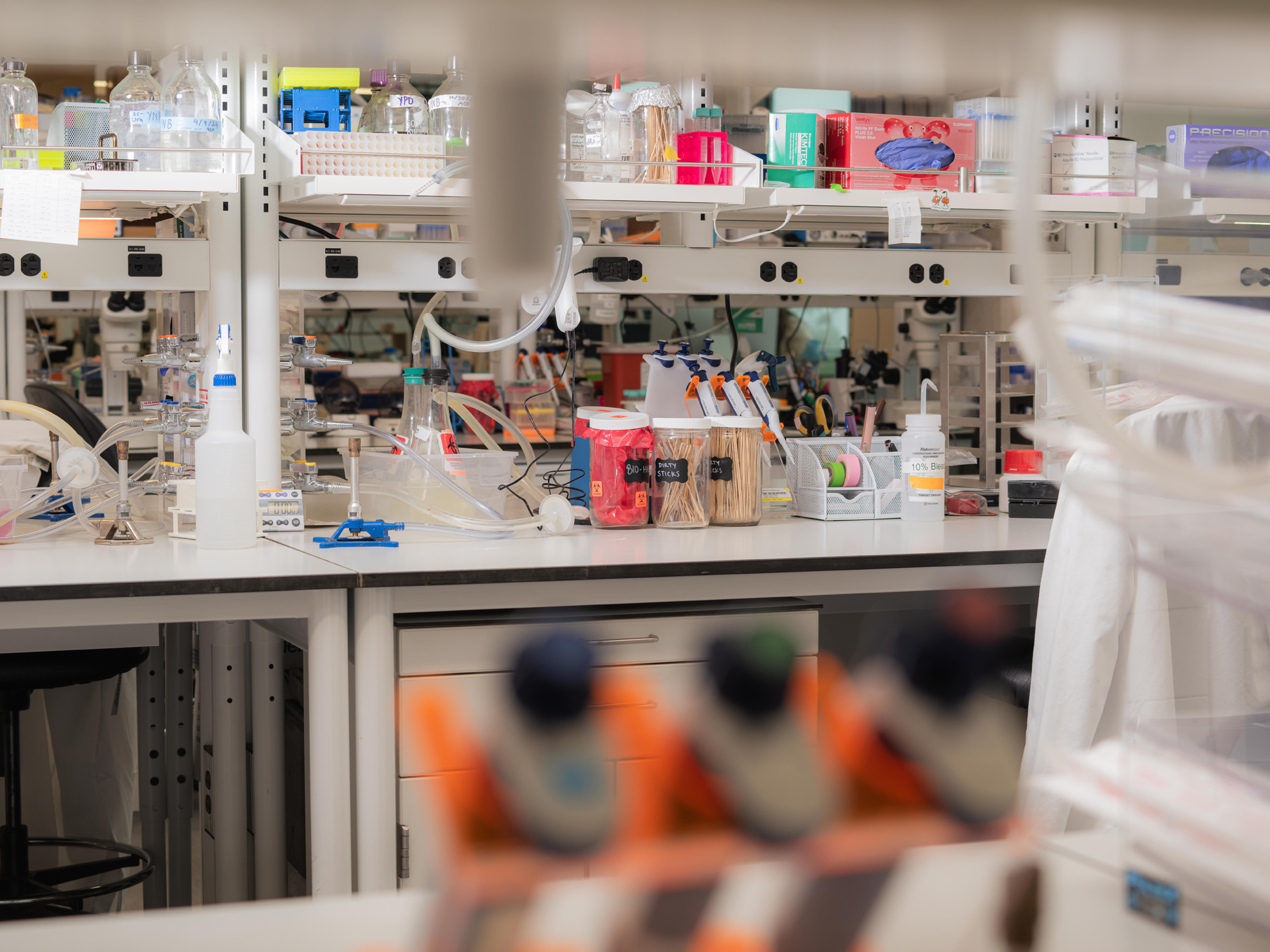 The counter in a scientific laboratory is full of test tubes and canisters full of materials, above is a row of evenly spaced charge ports.